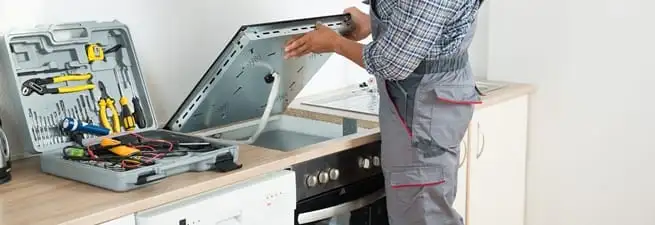 Cooktop repair technician lifting a built-in stovetop for service in Green Bay, WI
