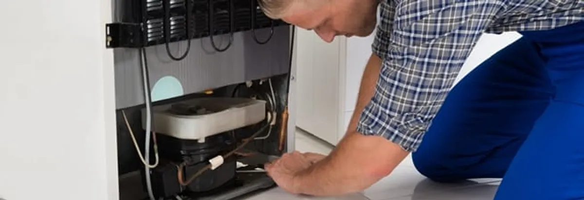 Refrigerator repair technician servicing the compressor and condenser area in Green Bay, WI