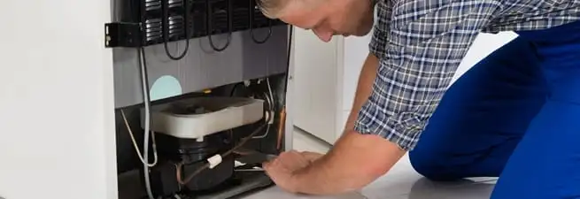 Refrigerator repair technician servicing the compressor and condenser area in Green Bay, WI