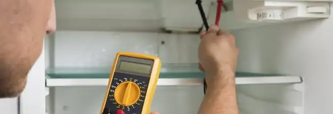 Refrigerator repair technician testing electrical components with a multimeter in Green Bay, WI