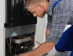 Refrigerator repair technician servicing the compressor and condenser area in Green Bay, WI